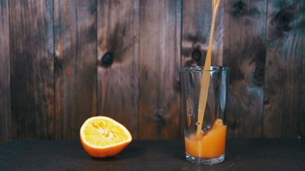 Orange Juice töltött egy pohárba, egy fából készült háttér. Lassú mozgás — Stock videók