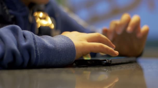 Manos del niño jugando con el teléfono móvil en la mesa — Vídeo de stock