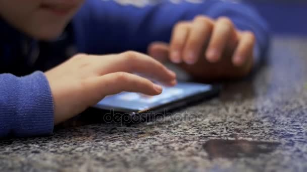 Niño jugando con el teléfono móvil en la mesa — Vídeos de Stock
