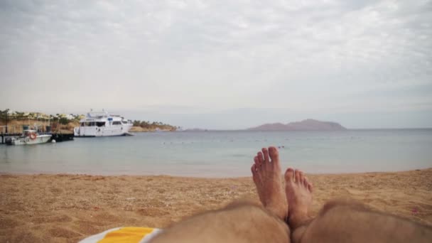 Gambe dell'uomo sdraiato sulla spiaggia lettino vicino al mare — Video Stock