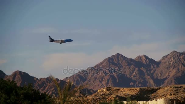 Avión de pasajeros en el cielo Aterrizaje en el fondo de las montañas y palmeras en Egipto. Moción lenta — Vídeo de stock