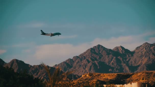 Avión de pasajeros en el cielo Aterrizaje en el fondo de las montañas y palmeras en Egipto. Moción lenta — Vídeos de Stock