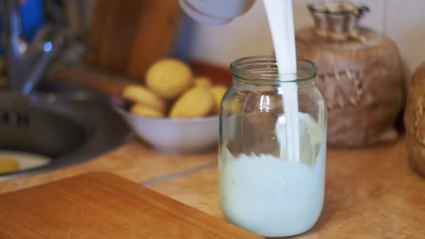 Mjölken hälls i en genomskinlig burk på en bakgrund av hem kök. Slow Motion — Stockvideo