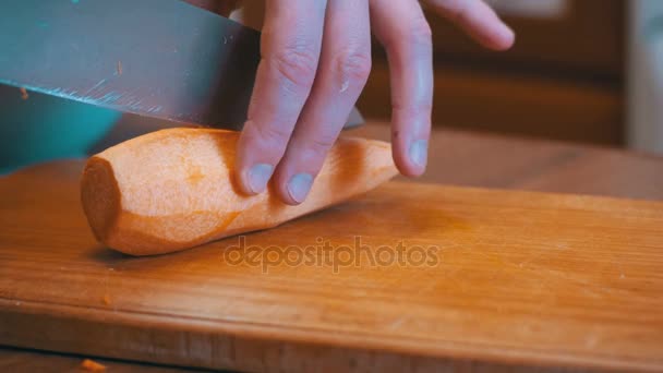 Γυναίκα χέρια με ένα μαχαίρι σε φέτες καρότο με μαχαίρι σε ένα ταμπλό με ξύλινο κουζίνα σε μια κουζίνα στο σπίτι — Αρχείο Βίντεο