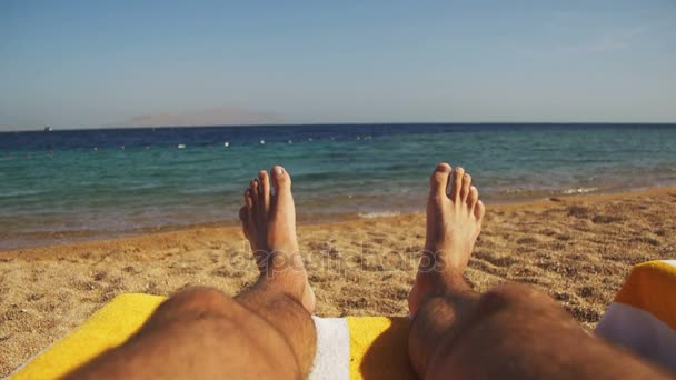 Beine des Mannes liegen auf Strandliegen in der Nähe des Meeres — Stockvideo