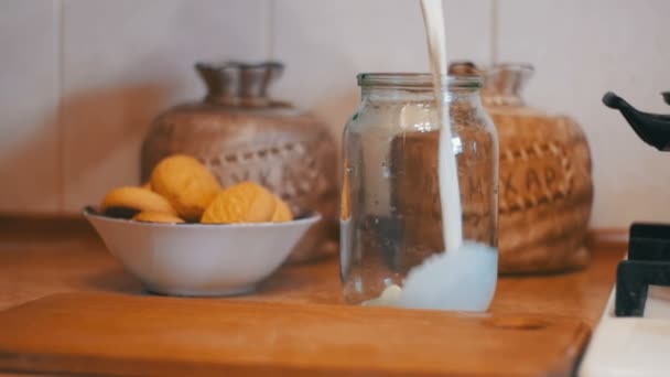 Milch wird in eine transparente Bank auf einem Hintergrund der heimischen Küche gegossen. Zeitlupe — Stockvideo