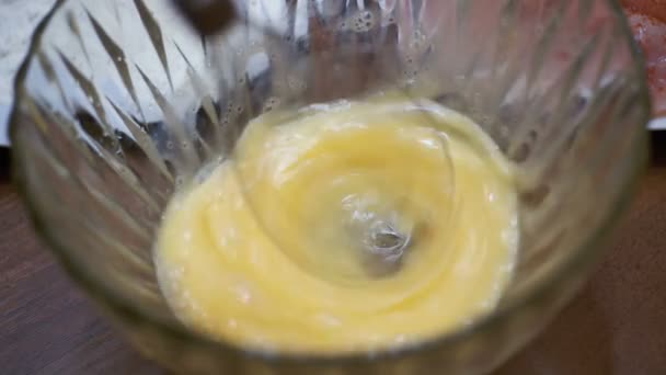 Взбивание яиц в прозрачной чаше с электрическим миксером для рук в медленном движении — стоковое видео
