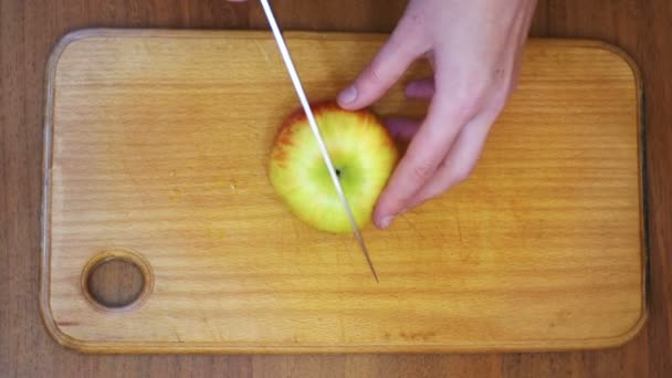 Manos de mujer con un cuchillo en rodajas de manzana en un tablero de cocina de madera en una cocina casera — Vídeo de stock