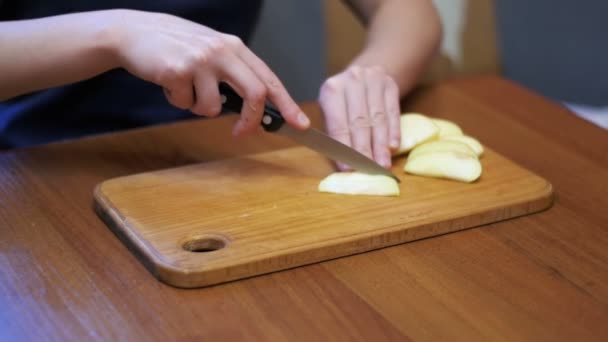 Mãos de mulher com uma faca de maçã fatiada em uma placa de cozinha de madeira em uma cozinha doméstica. Movimento lento — Vídeo de Stock