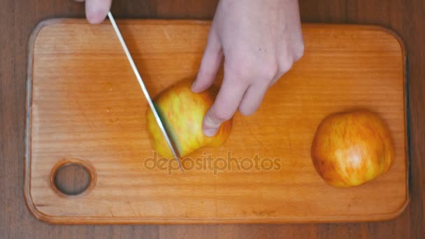 Manos de mujer con un cuchillo en rodajas de manzana en un tablero de cocina de madera en una cocina casera — Vídeos de Stock