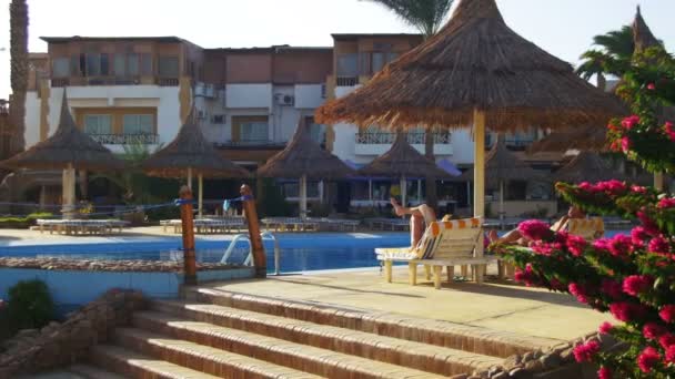 青いプール、ヤシの木、エジプトでサンベッドとホテル リゾートのプールサイドのラウンジャーで日光浴の人 — ストック動画