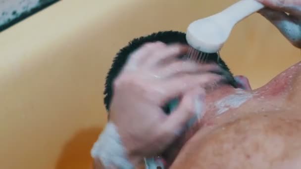 Молодой человек моет голову шампунем под душем — стоковое видео