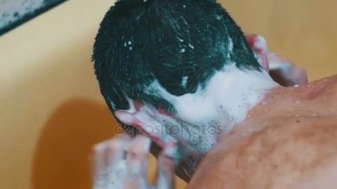 Genç adam kafasını duş altında şampuanla yıkar