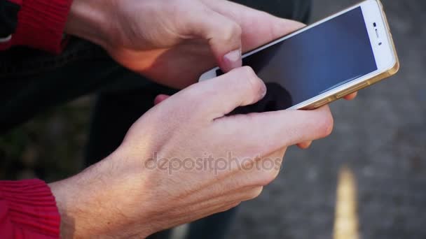 Νεαρός χρησιμοποιώντας ένα κινητό τηλέφωνο σε ένα παγκάκι στο πάρκο της πόλης — Αρχείο Βίντεο