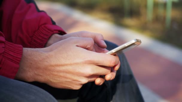 Ung Man med hjälp av en mobiltelefon på en bänk i stadsparken — Stockvideo