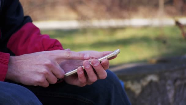 Ung Man med en Smartphone på en bänk i stadsparken — Stockvideo