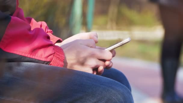 Jovem usando um telefone celular em um banco no parque da cidade — Vídeo de Stock