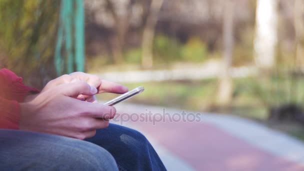 Jovem usando um telefone celular em um banco no parque da cidade — Vídeo de Stock