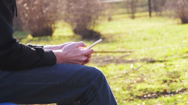 Menina usando um telefone celular em um banco no parque da cidade na primavera . — Vídeo de Stock