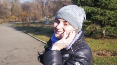 Gülümseyen ve yavaş şehir parkında bir smartphone cep telefonu ile konuşurken mutlu genç kız