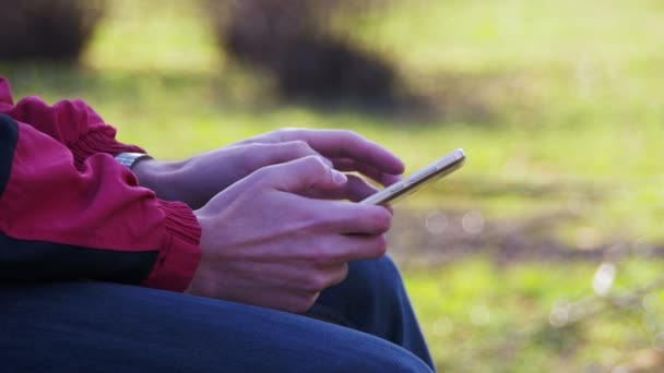 Молода людина, за допомогою мобільного телефону на лавці в парку міста — стокове відео