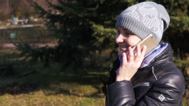 Chica joven feliz sonriendo y hablando en un teléfono inteligente en el parque de la ciudad en cámara lenta — Vídeos de Stock