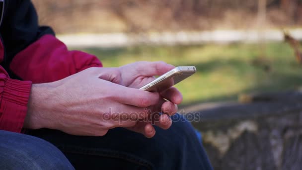 Ung Man med hjälp av en mobiltelefon på en bänk i stadsparken — Stockvideo