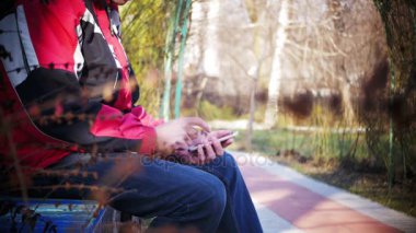 Genç şehir parkta bir bankta bir cep telefonu kullanan adam