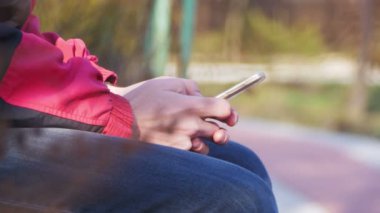 Kent parkta bir bankta bir akıllı telefon kullanan genç adam