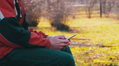 Kent parkta bir bankta bir akıllı telefon kullanan genç adam