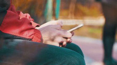 Kent parkta bir bankta bir akıllı telefon kullanan genç adam
