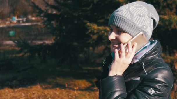 Gülümseyen ve yavaş şehir parkında bir smartphone cep telefonu ile konuşurken mutlu genç kız — Stok video