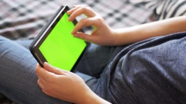 Genç kadın Lying yatak ve Tablet Yeşil perde ile evde kullanma.
