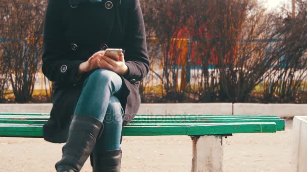 Junges Mädchen mit Handy auf einer Bank im Stadtpark — Stockvideo