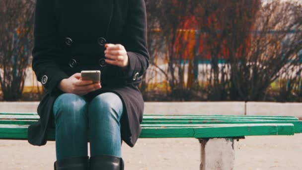 Ung flicka med en mobiltelefon på en bänk i stadsparken — Stockvideo