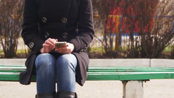 Menina usando um telefone celular em um banco no parque da cidade — Vídeo de Stock