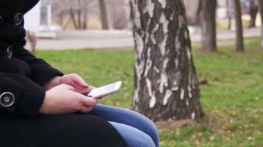 Genç şehir parkta bir bankta bir akıllı telefon kullanan kadın