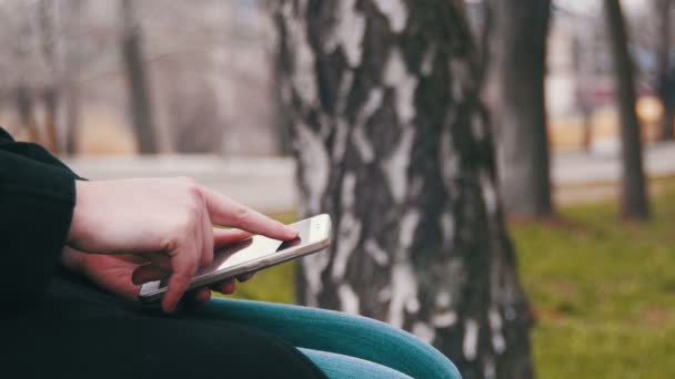 Jonge vrouw met behulp van een Smartphone op een bankje in het Park van de stad — Stockvideo