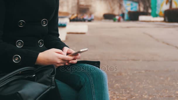 Chica usando un teléfono móvil en un banco en el parque de la ciudad en la primavera . — Vídeos de Stock