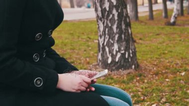 Genç kadın şehir parkta bir bankta bir cep telefonu kullanarak