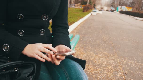 Jeune femme utilisant un Smartphone sur un banc dans le parc de la ville — Video