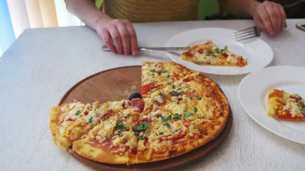 A menina está comendo uma pizza em uma placa branca em um restaurante em uma mesa de madeira branca. Dolly Shot — Vídeo de Stock