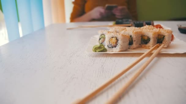 Женщина в японском ресторане и тарелки суши-роллов на белом стильном деревянном столе. Долли Шот — стоковое видео