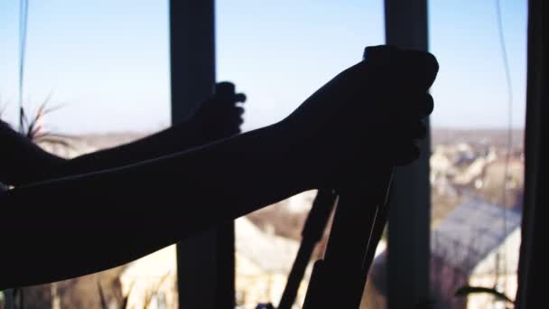 Mujer joven ejercitándose en la máquina elíptica en casa contra la ventana — Vídeo de stock