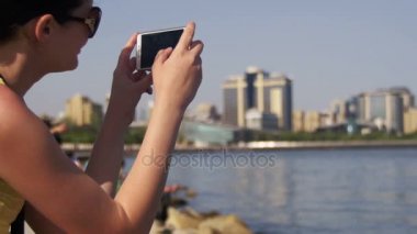 Genç kadın almak resmi Smartphone oturan için setin yakınındaki Megapolis gökdelenler ve deniz