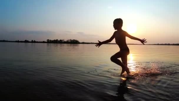 Het kind loopt langs het strand in de achtergrond van de zonsondergang. Slow Motion — Stockvideo