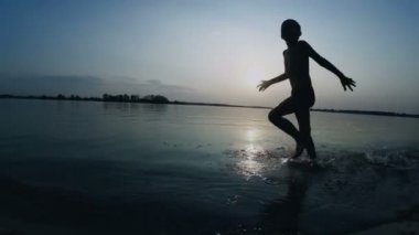 Mutlu çocuk gün batımında kumsal boyunca çalışır. Ağır çekim