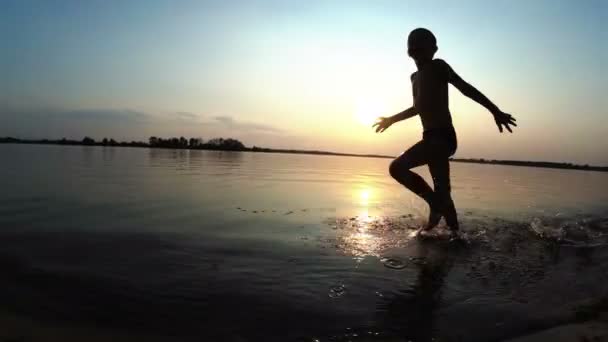 Ευτυχισμένο παιδί τρέχει κατά μήκος της παραλίας στο ηλιοβασίλεμα. Αργή κίνηση — Αρχείο Βίντεο
