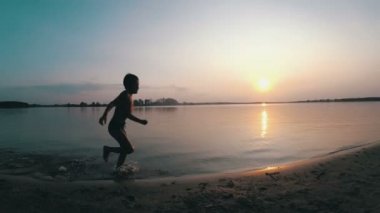 Mutlu çocuk gün batımında kumsal boyunca çalışır. Ağır çekim