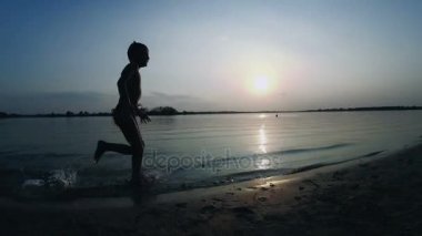 Gün batımında kumsal boyunca çalışan mutlu çocuk silüeti. Ağır çekim